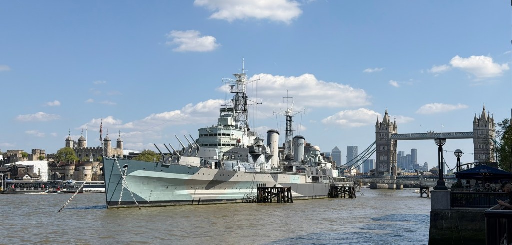 Photograph taken April 2026 showing HMS Belfast moored on the River Thames. The Tower of London and Tower Bridge ​are also in shot.